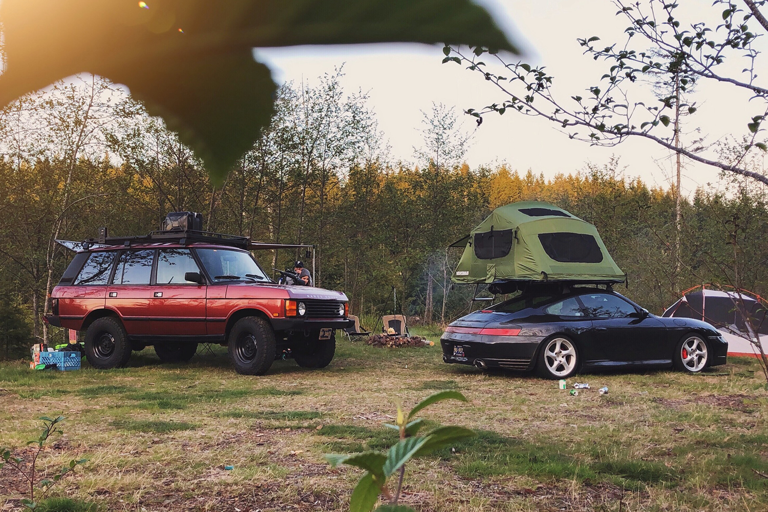 A 1991 red Range Rover Classic and black Porsche 996 with a car camping tent