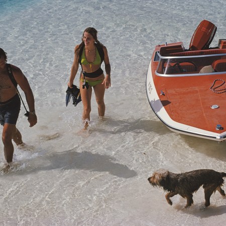 A man and woman return from snorkeling with their dog and boat on a tropical beach.
