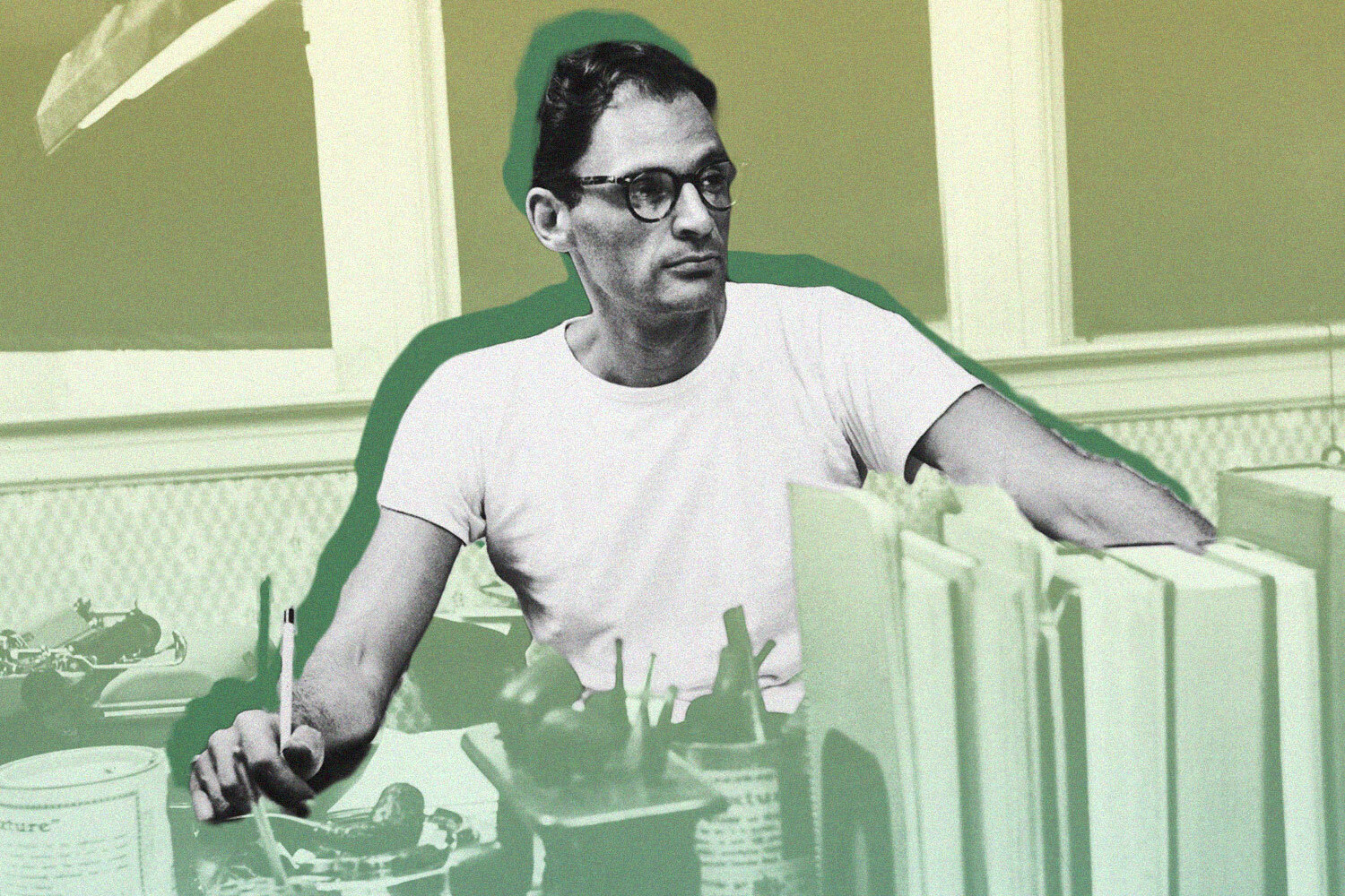 Arthur Miller seated at his desk, pen in hand, surrounded by books — fully engaged in the act of writing.