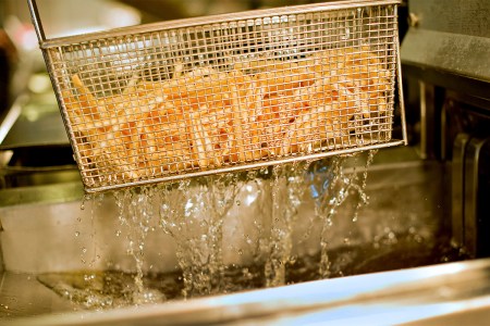 French fries being lifted from a deep fryer filled with hot cooking oil