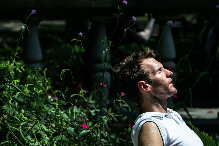 Man sitting in sunlight with eyes closed, reflecting in a quiet garden.